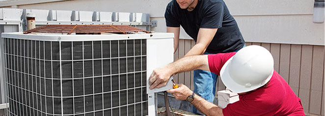 Two workers on the roof of a building working on the air conditioning unit.