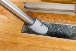Horizontal photo of vacuum cleaning inside heater floor vent with Red Oak Floors in background
